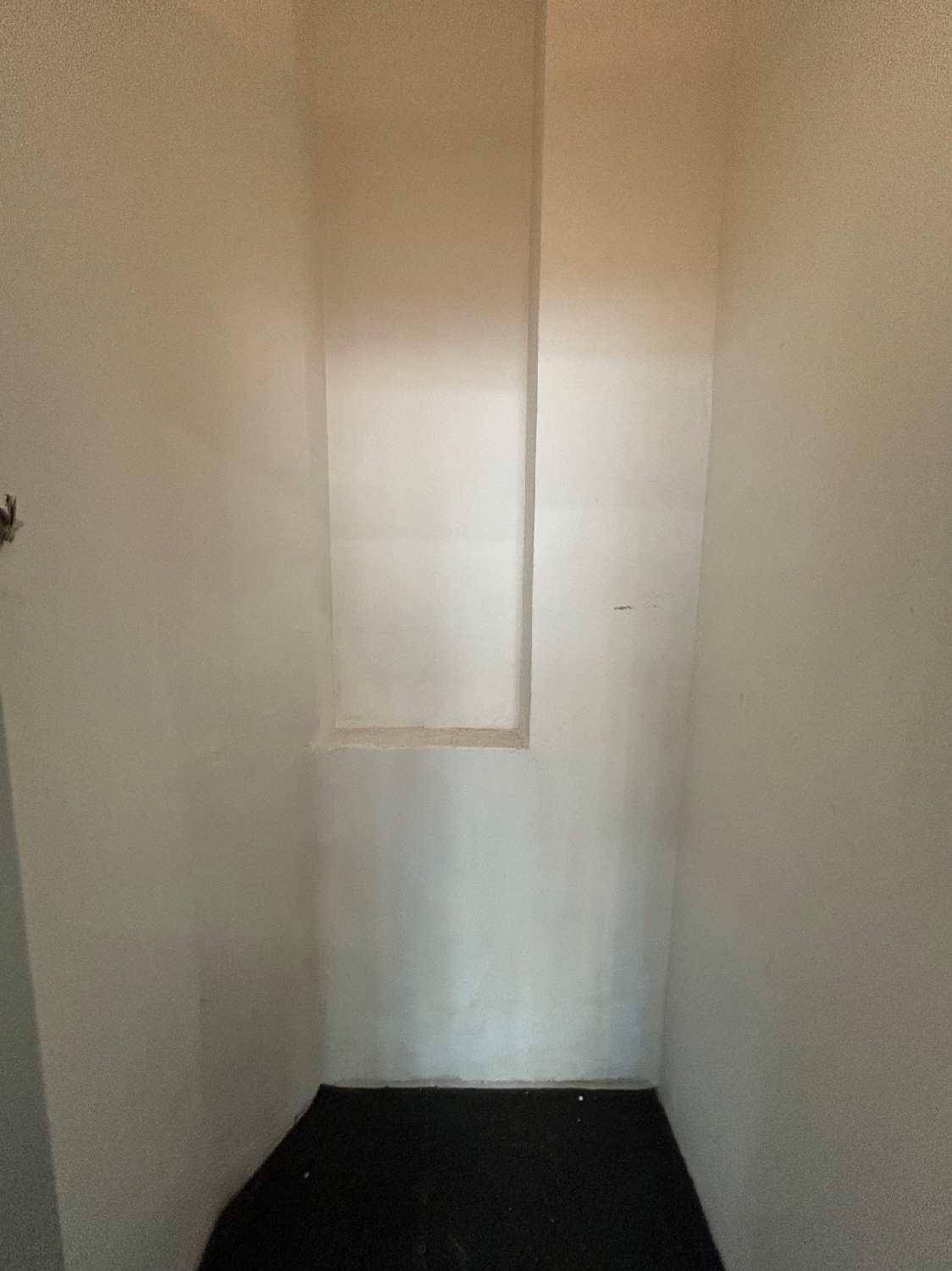 Kleiner, schmaler Raum mit weißen Wänden und dunklem Boden, möglicherweise als Abstellraum nutzbar.