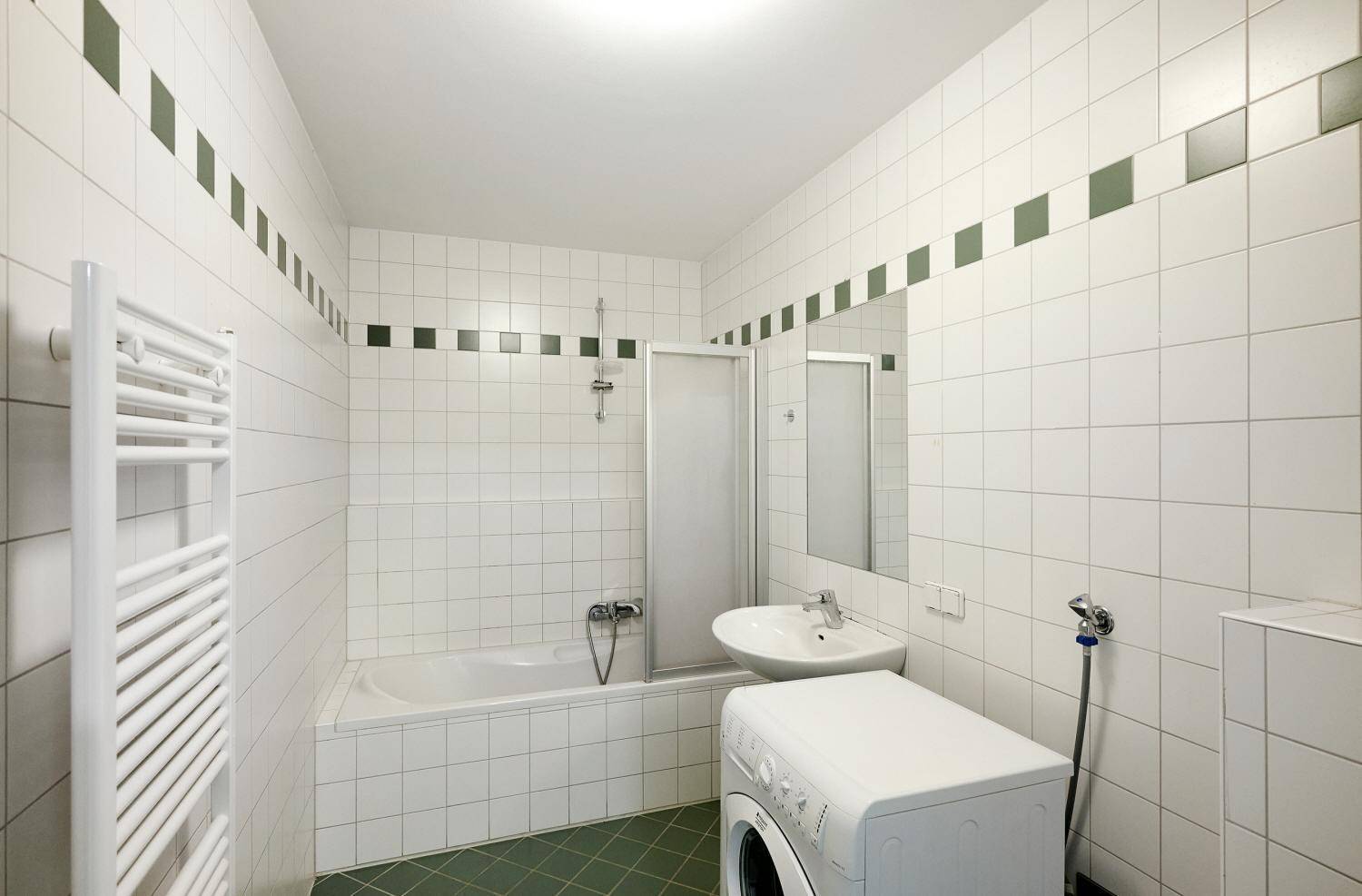 Gefliestes Badezimmer mit Badewanne, Dusche, Waschbecken und beheiztem Handtuchhalter.