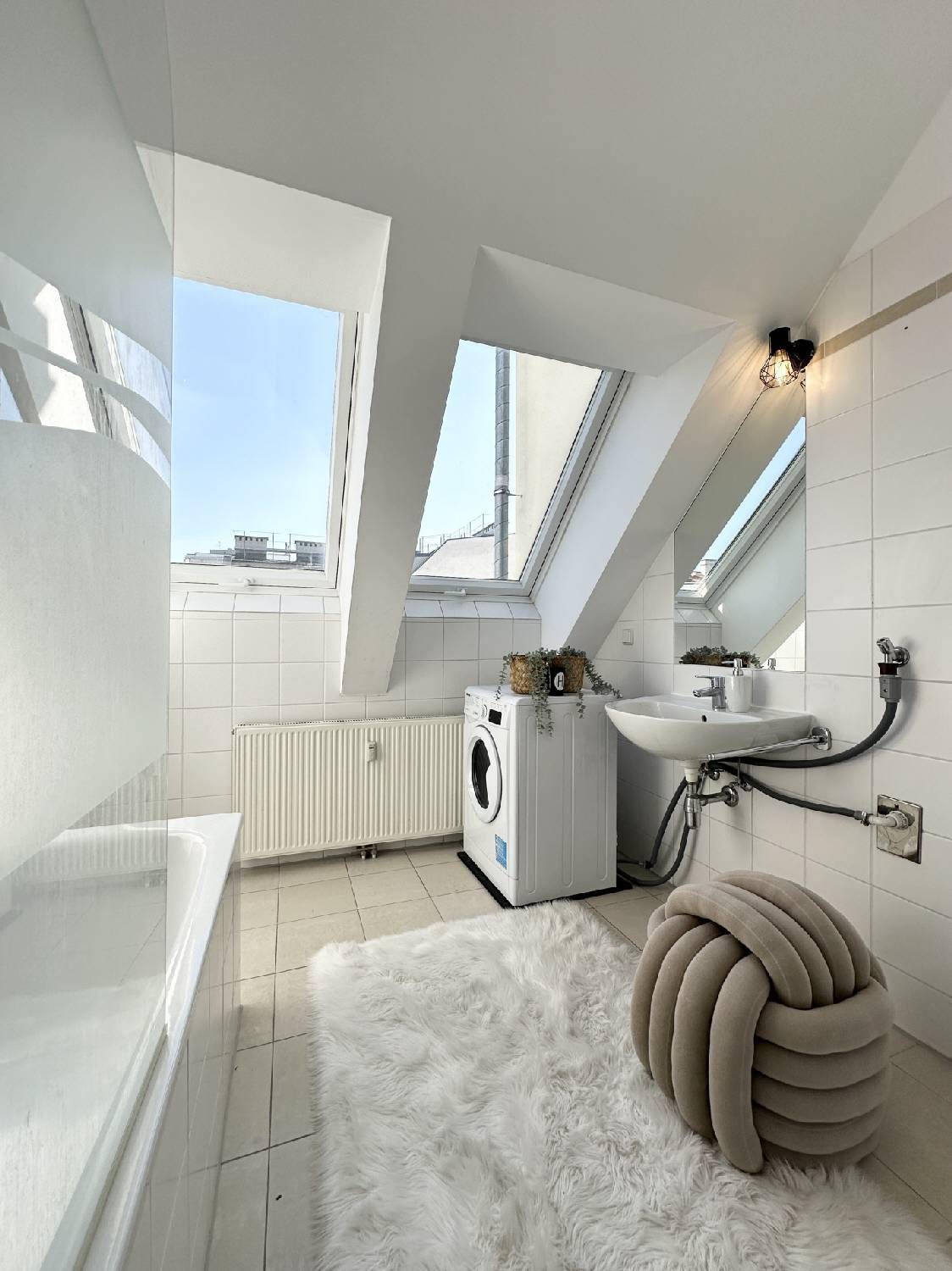 Helles Badezimmer mit Badewanne, Waschbecken, Waschmaschine und Dachfenstern.