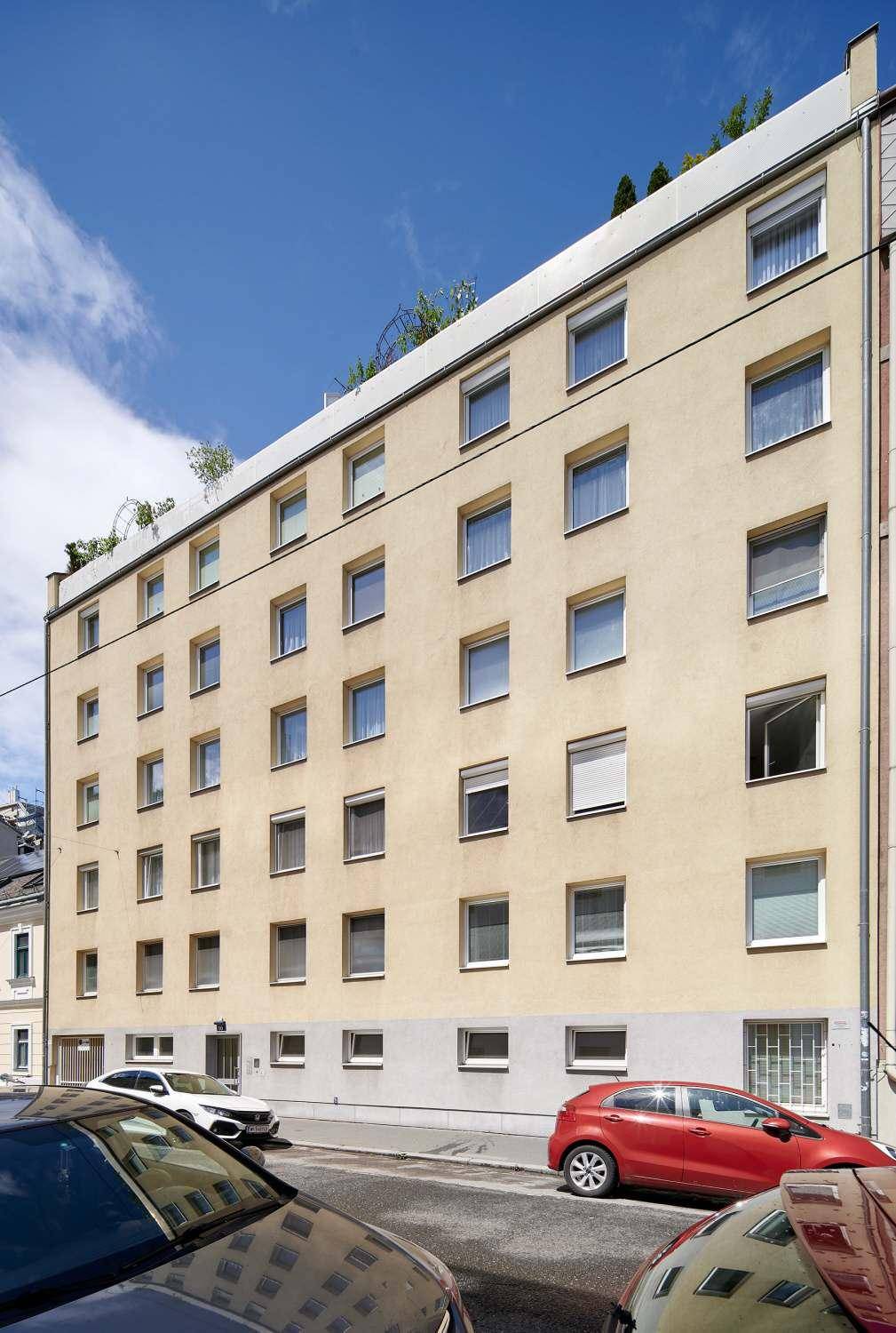 Ansicht der Gebäudefassade eines Mehrfamilienhauses mit zahlreichen Fenstern und sonnigem Wetter.