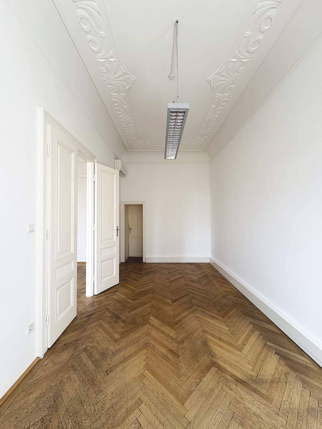 Langes Zimmer mit Fischgrätparkett und Stuckdecke, durchflutet von Tageslicht, mit mehreren Türen.