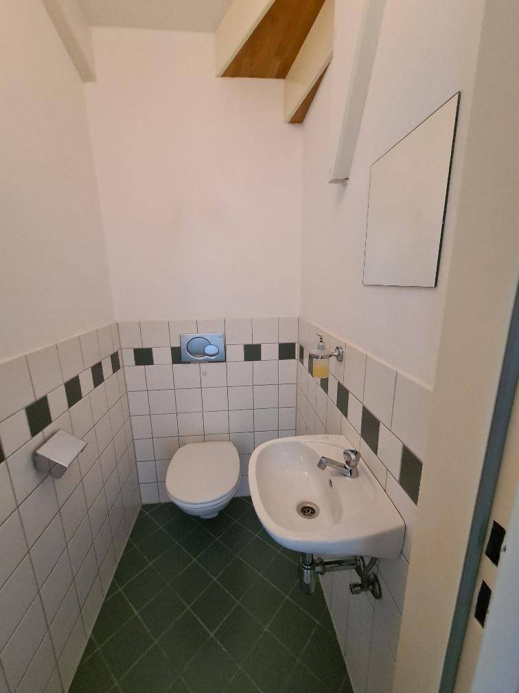 Kleines Gäste-WC mit weißen und grünen Fliesen, Toilette und einem Waschbecken.
