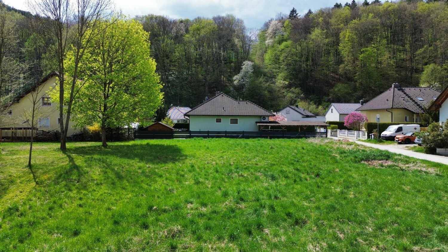 Weitläufiges grünes Grundstück mit einem Haus im Hintergrund und einem bewaldeten Hügel.