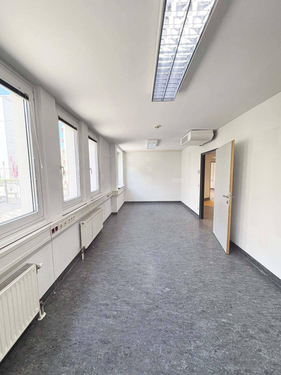 Geräumiger Bürobereich mit durchgehender Fensterfront und grauem Linoleumboden.
