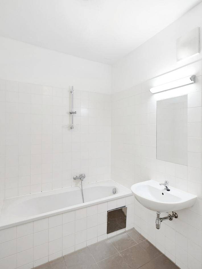 Helles Badezimmer mit weiß gefliesten Wänden, Badewanne und Waschbecken.