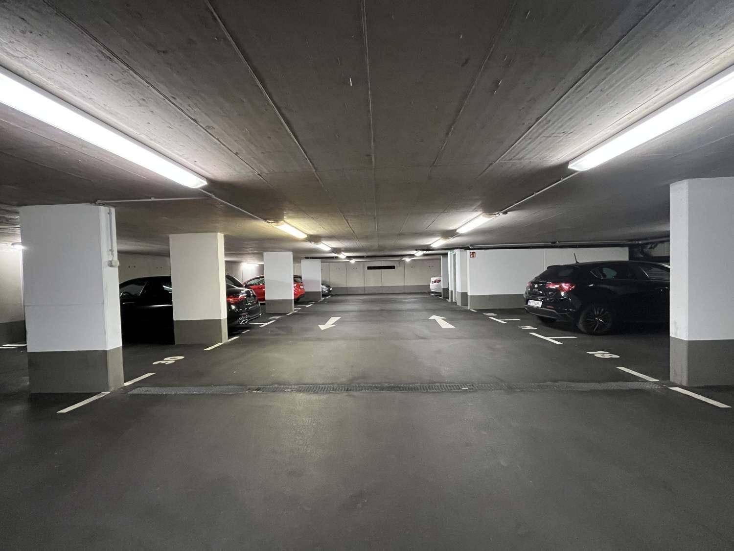 Helle Tiefgarage mit zahlreichen Stellplätzen, Betonpfeilern und durchgehender Beleuchtung.