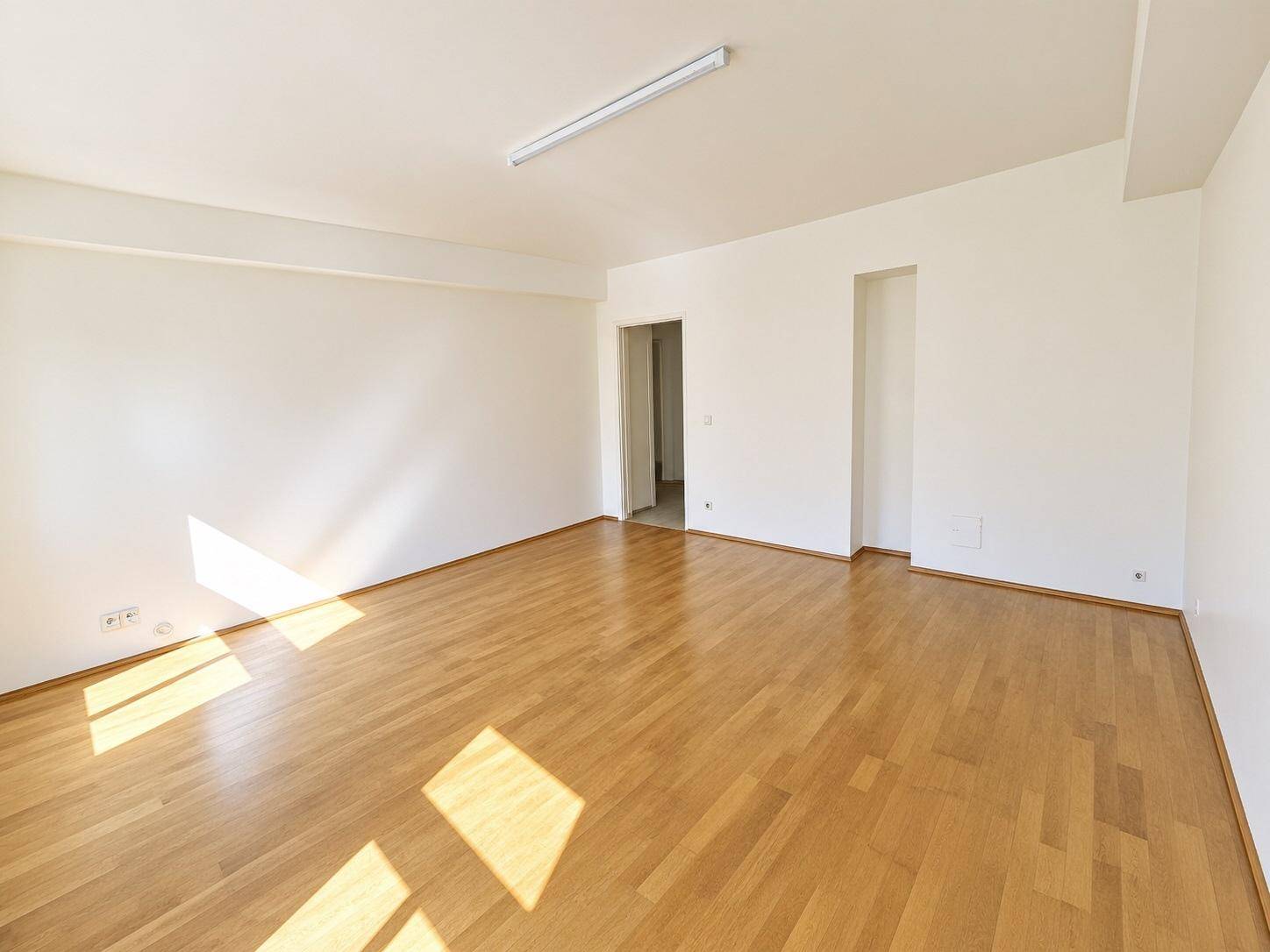 Geräumiges, helles Zimmer mit Parkettboden und Zugang zu einem weiteren Raum, ideal für flexible Nutzung.