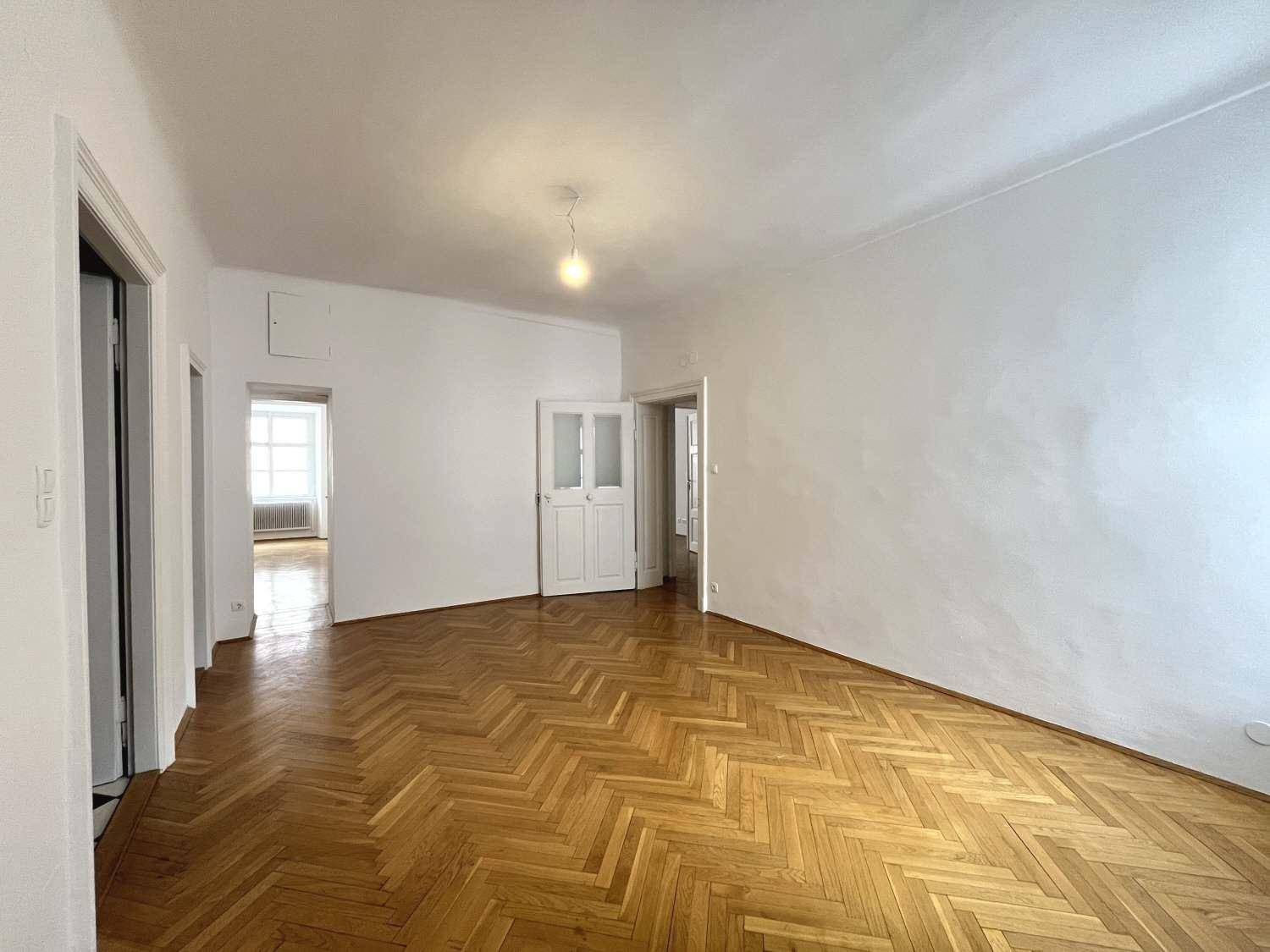 Geräumiges Zimmer mit Fischgrätparkett und Zugang zu weiteren Räumen durch Flügeltüren.