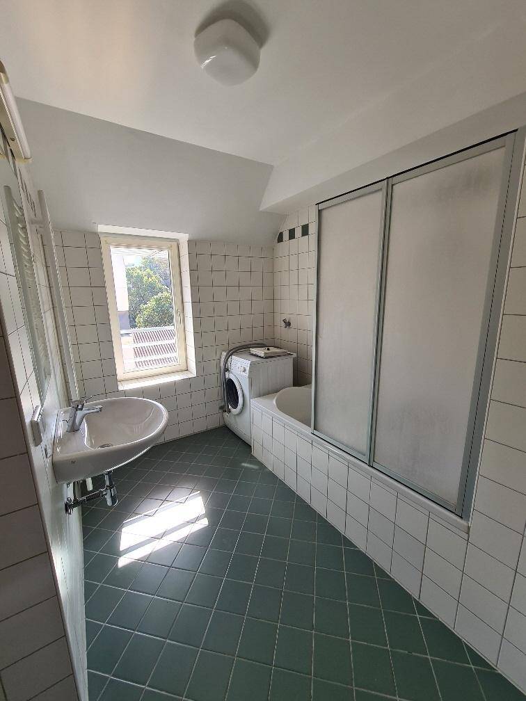 Badezimmer mit weißen und grünen Fliesen, Badewanne mit Duschwand und Waschmaschine, inklusive Fenster.