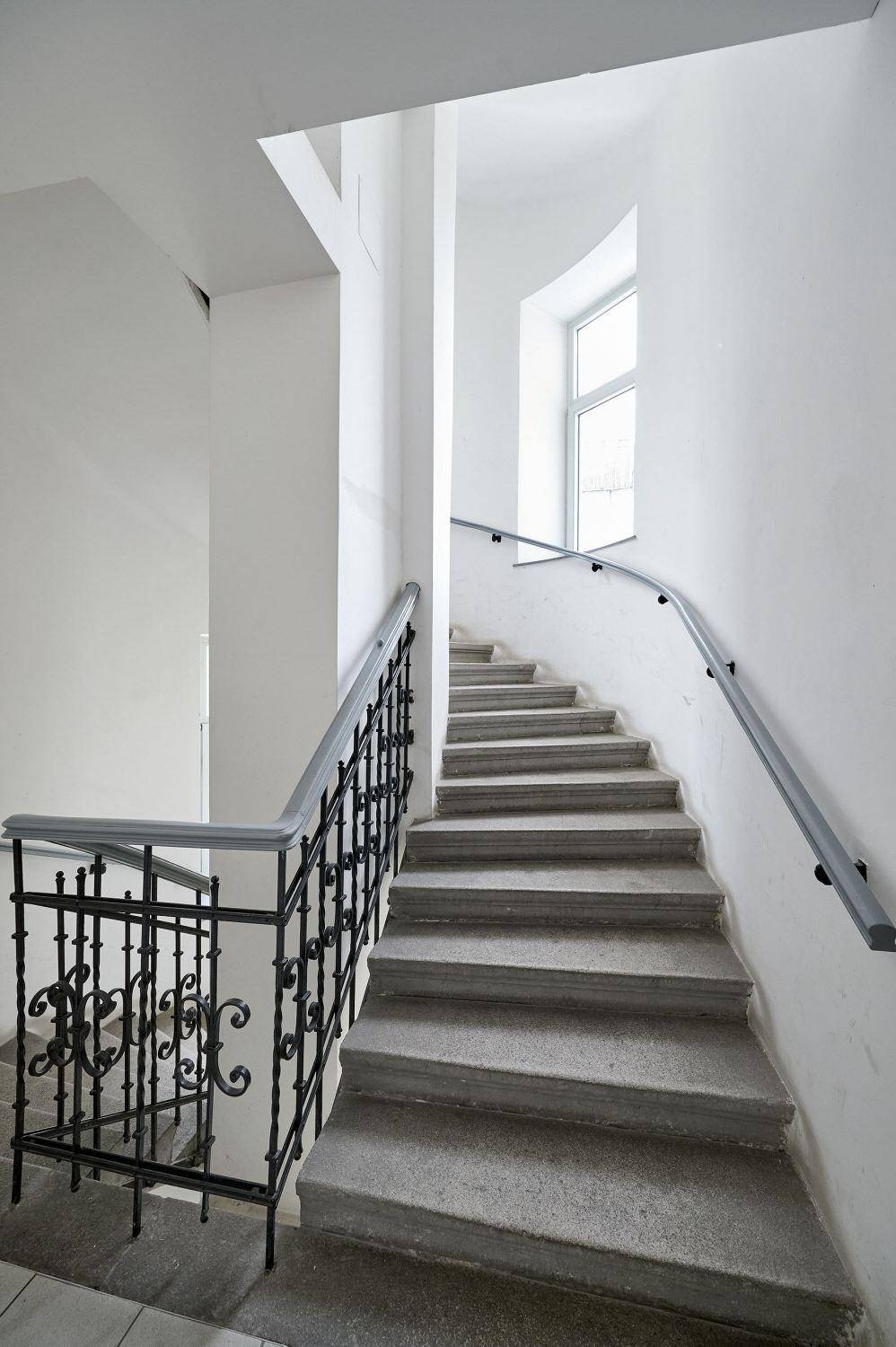 Treppenhaus mit Steinstufen und einem verzierten schmiedeeisernen Geländer.