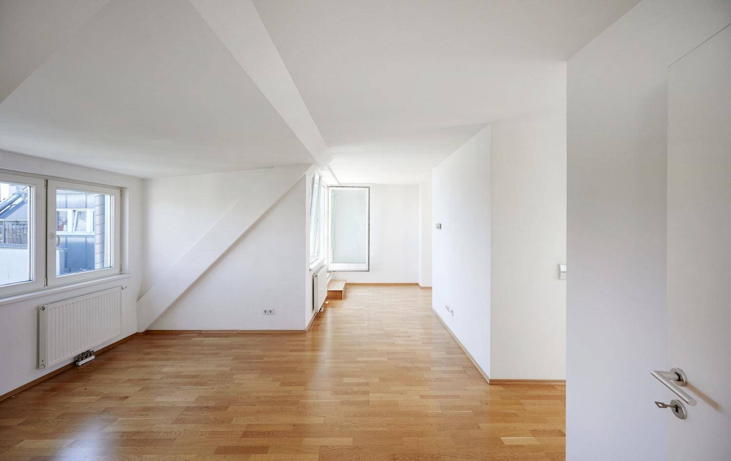 Großes, helles Wohnzimmer im Dachgeschoss mit Holzboden und Zugang zum Balkon.