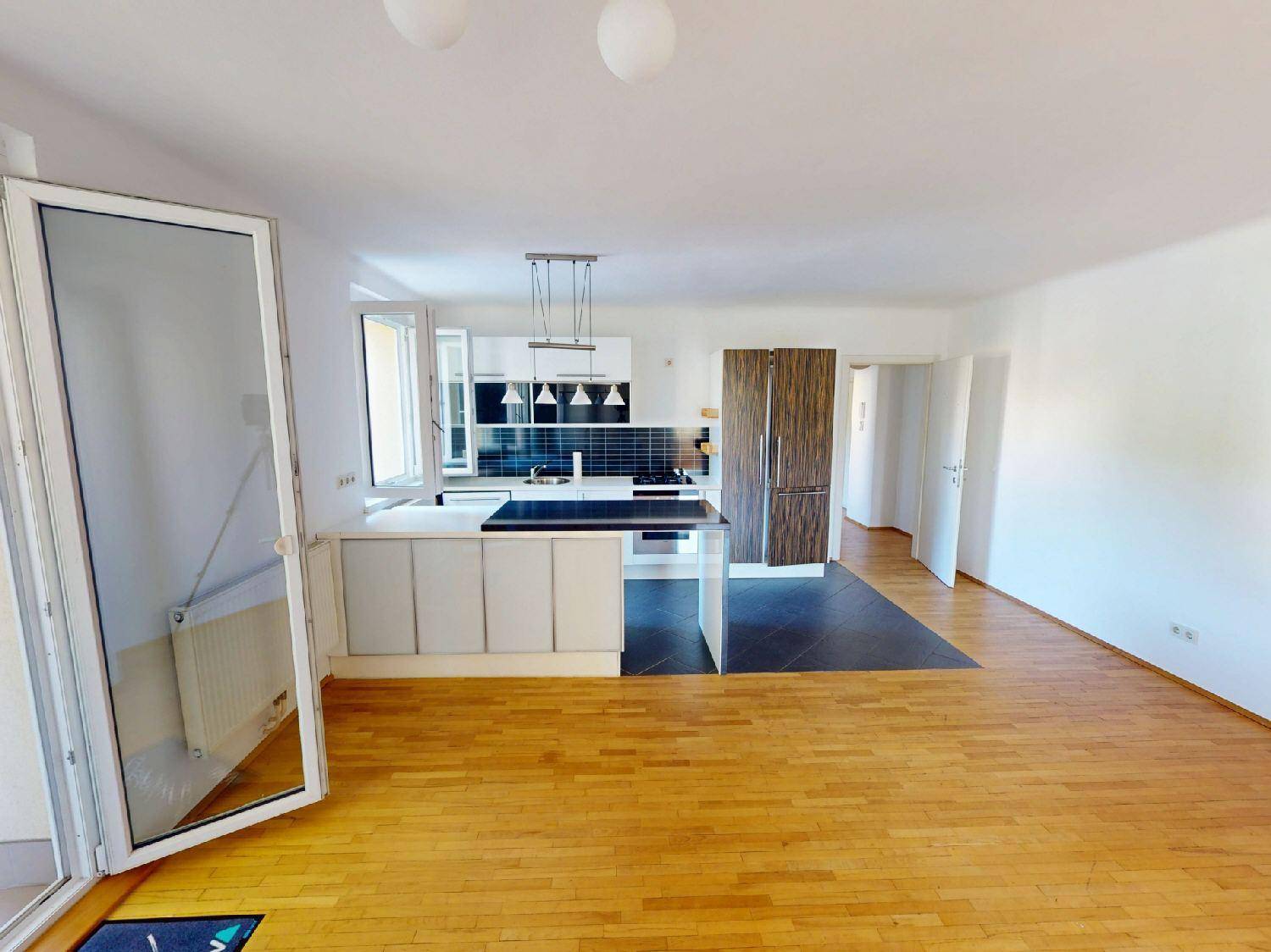 Heller Wohn- und Essbereich mit offener Küche, Parkettboden und Zugang zum Balkon.