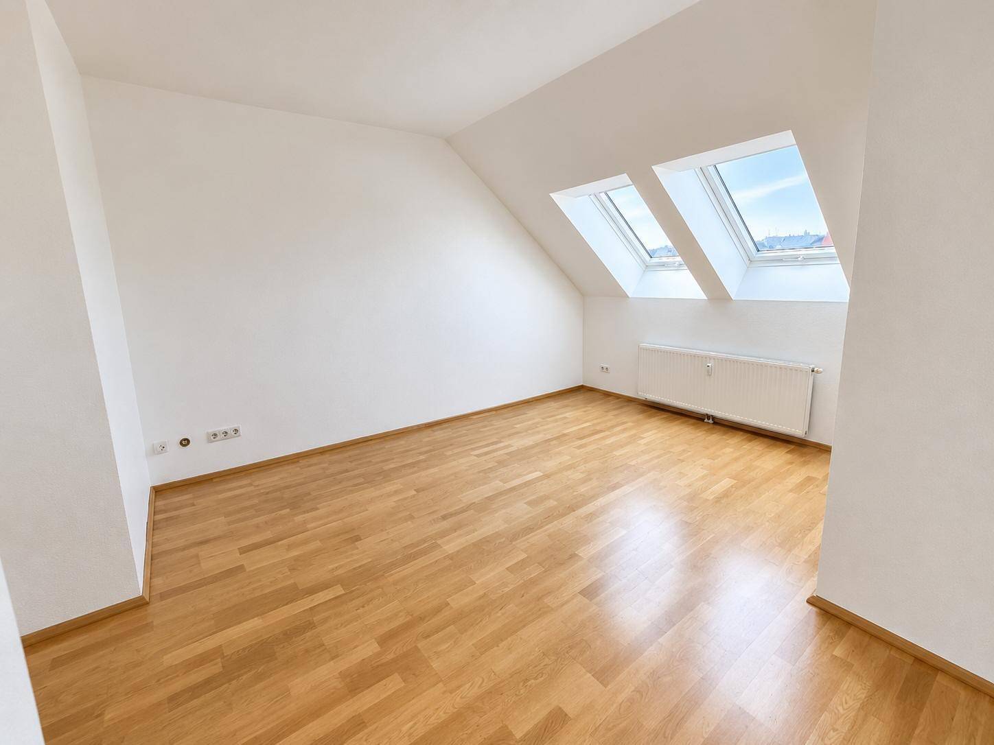 Geräumiges Zimmer im Dachgeschoss mit Holzboden und zwei Dachfenstern für viel Tageslicht.