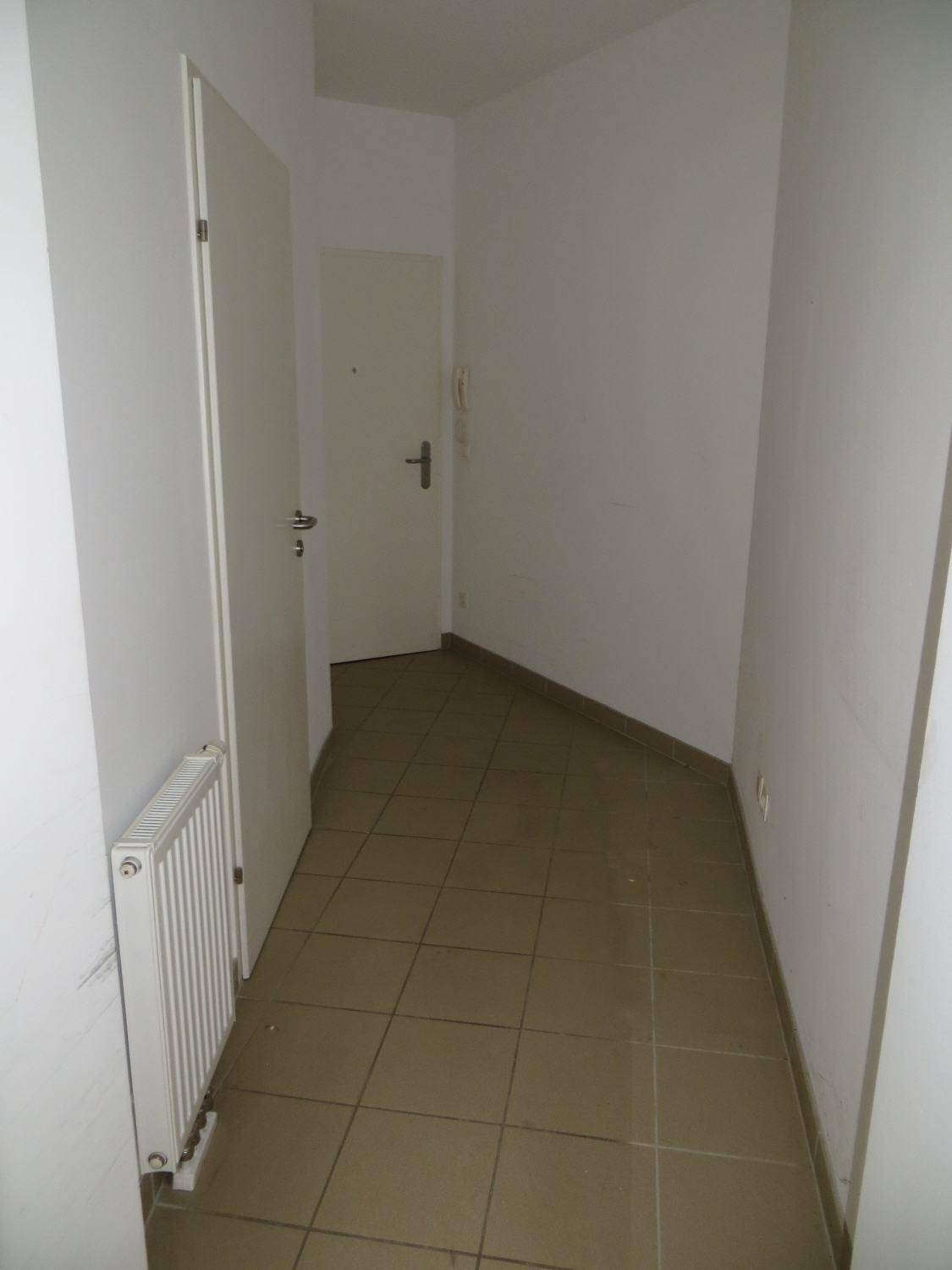 Langer Flur mit Fliesenboden, weiß gestrichenen Wänden und Heizkörper.