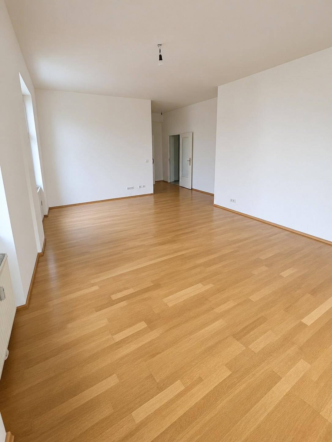 Weitläufiges, helles Zimmer mit Parkettboden und Blick auf den Flurbereich mit Türen.