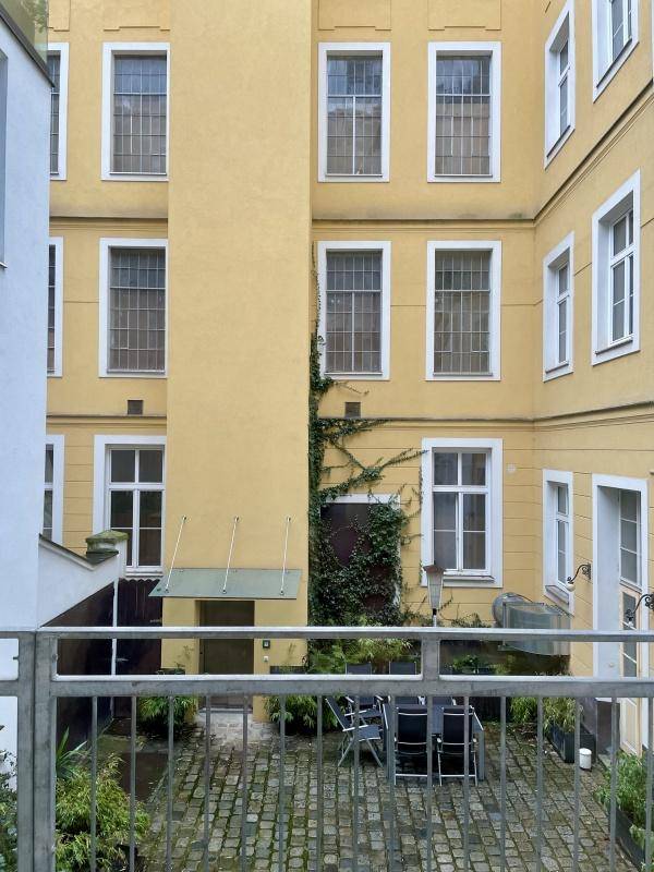 Detailansicht des begrünten Innenhofs von einem Balkon aus, mit gelber Gebäudefassade und Sitzmöbeln.