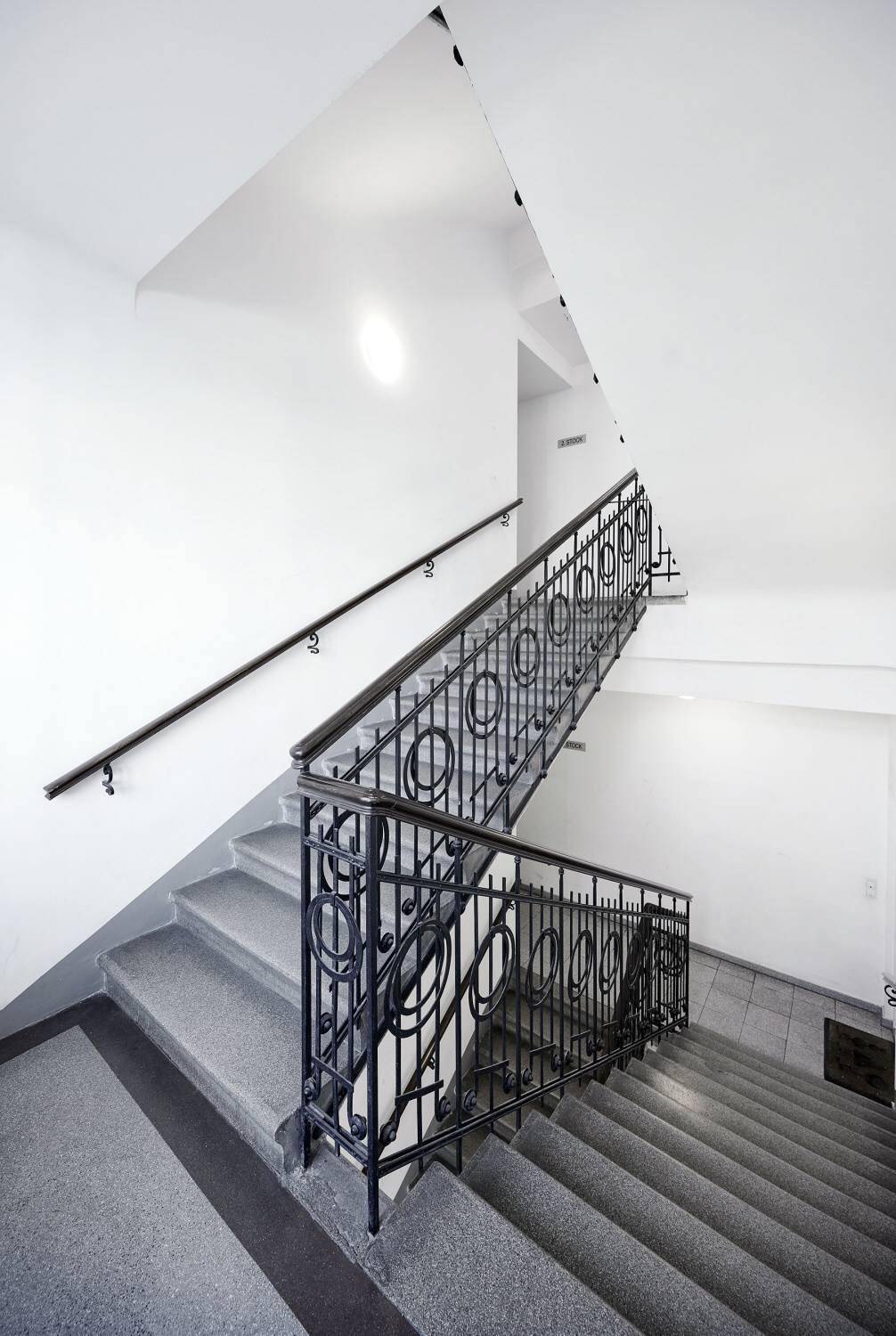 Treppenhaus mit elegantem schmiedeeisernem Geländer und hellen Wänden, das nach oben führt.