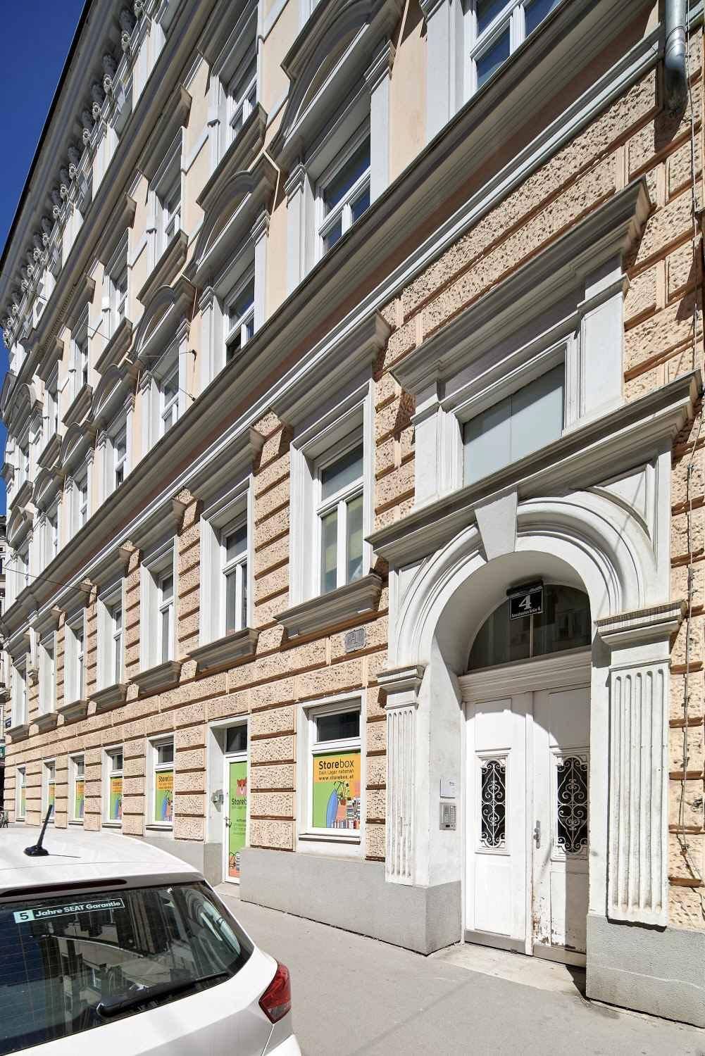 Historische Fassade eines Wohngebäudes mit Geschäften im Erdgeschoss und geparkten Autos.