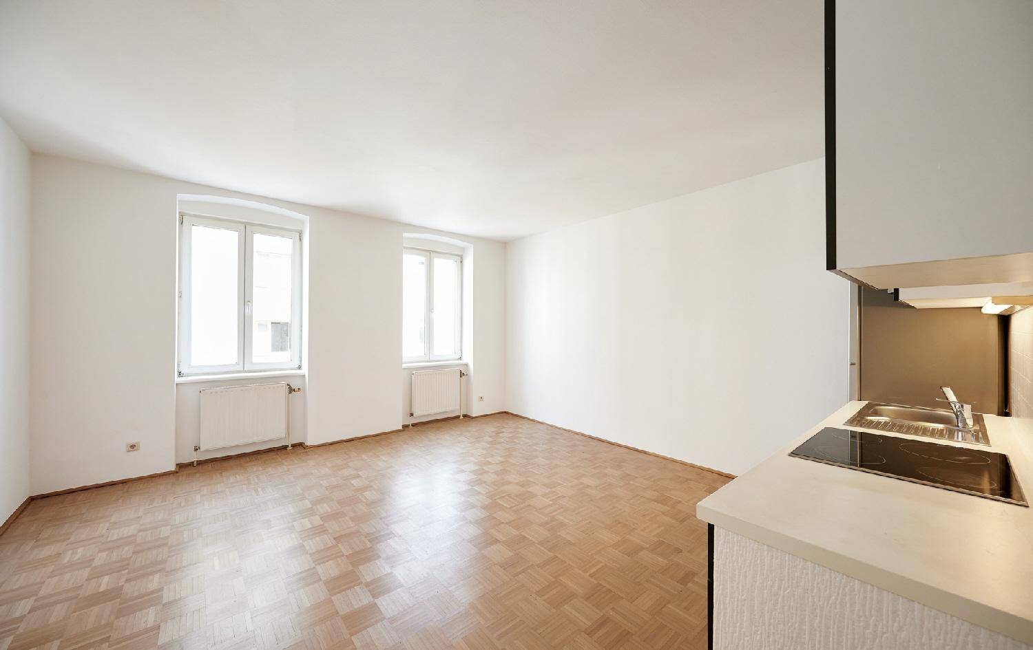 Heller Raum mit Parkettboden und integriertem Küchenbereich, ideal für offenes Wohnen.