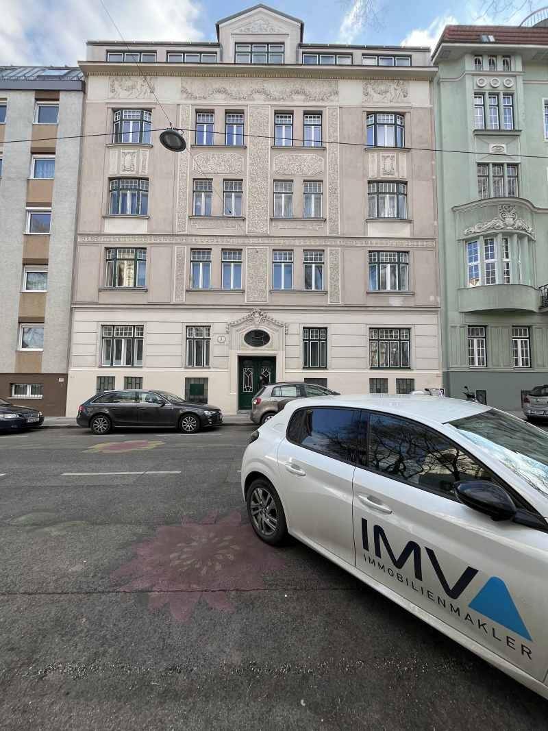 Ansicht der historischen Fassade eines Mehrfamilienhauses mit parkenden Autos auf der Straße.