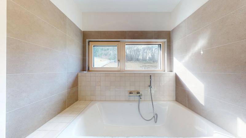 Eingebaute Badewanne unter einem Fenster in einem hell gefliesten Badezimmer.