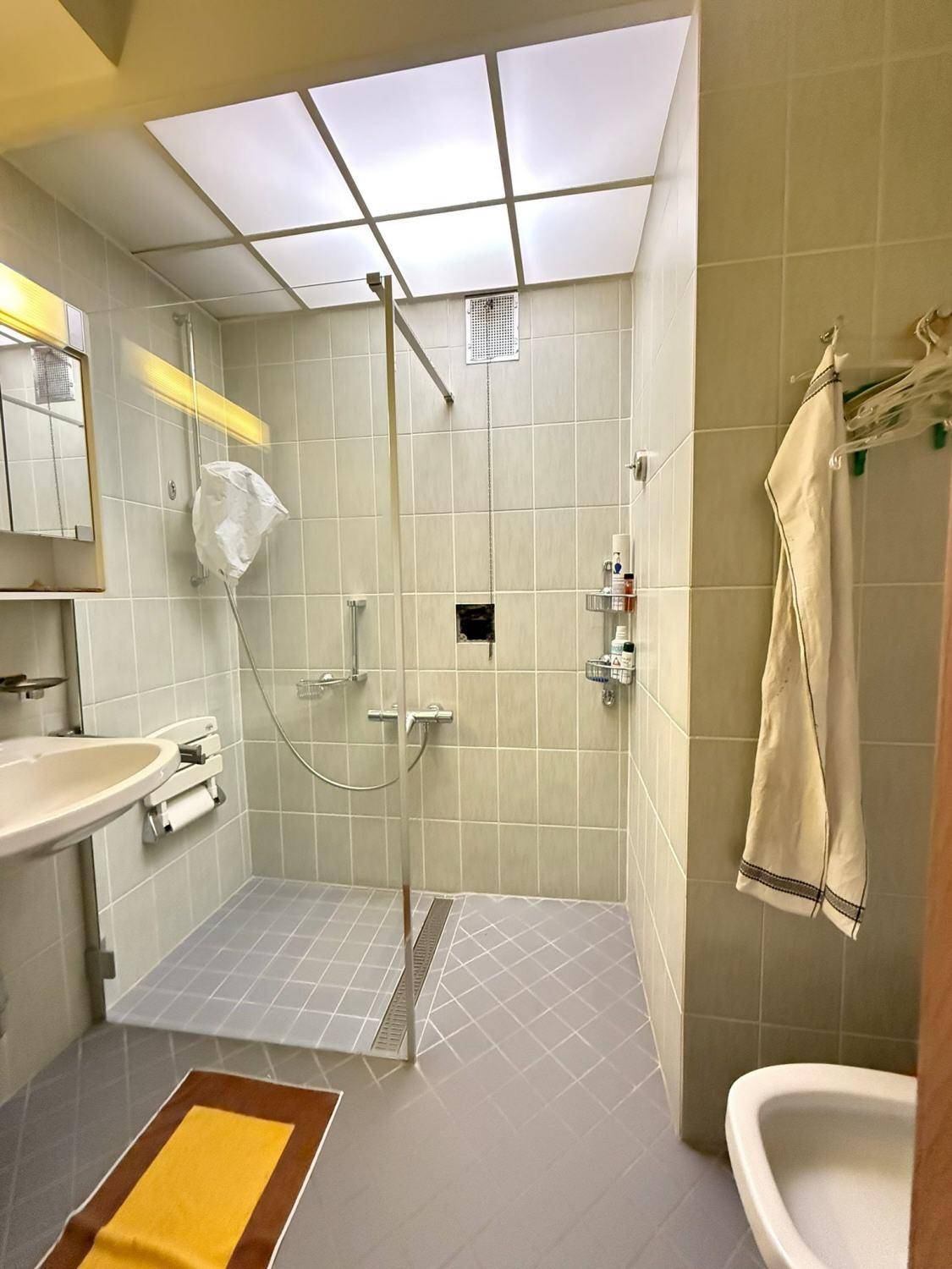 Badezimmer mit begehbarer Dusche, Waschbecken und hellen Fliesen an Wänden und Boden.