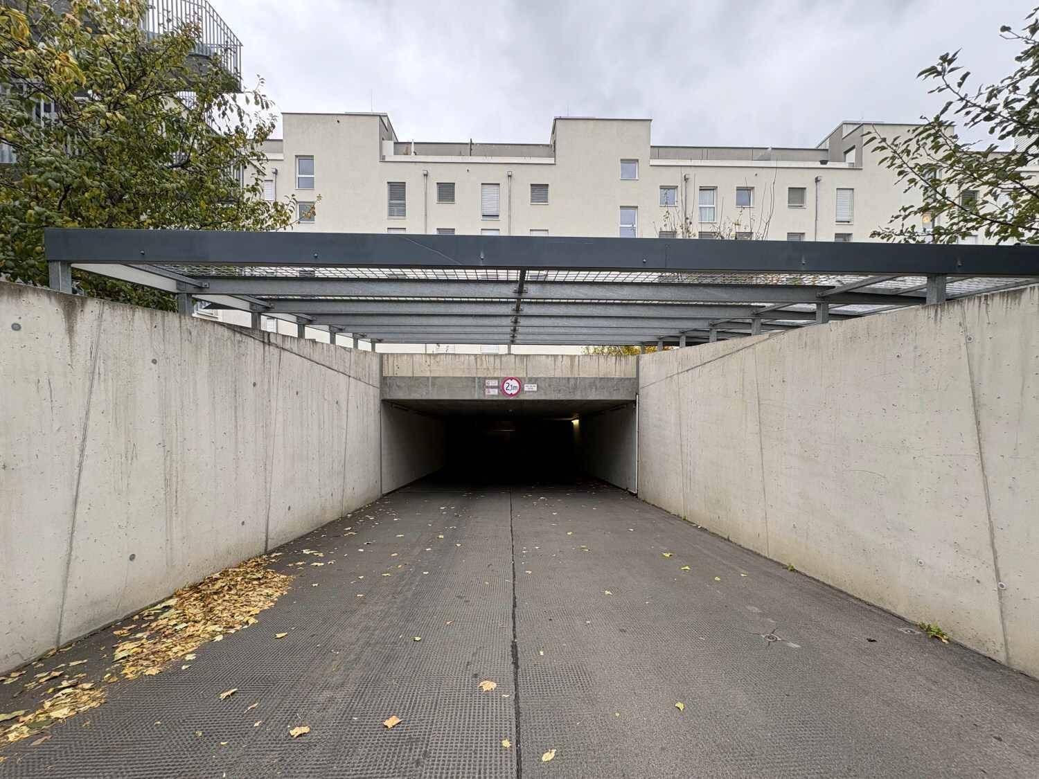 Einfahrt zur Tiefgarage mit Betonwänden und einem darüberliegenden Wohngebäude.