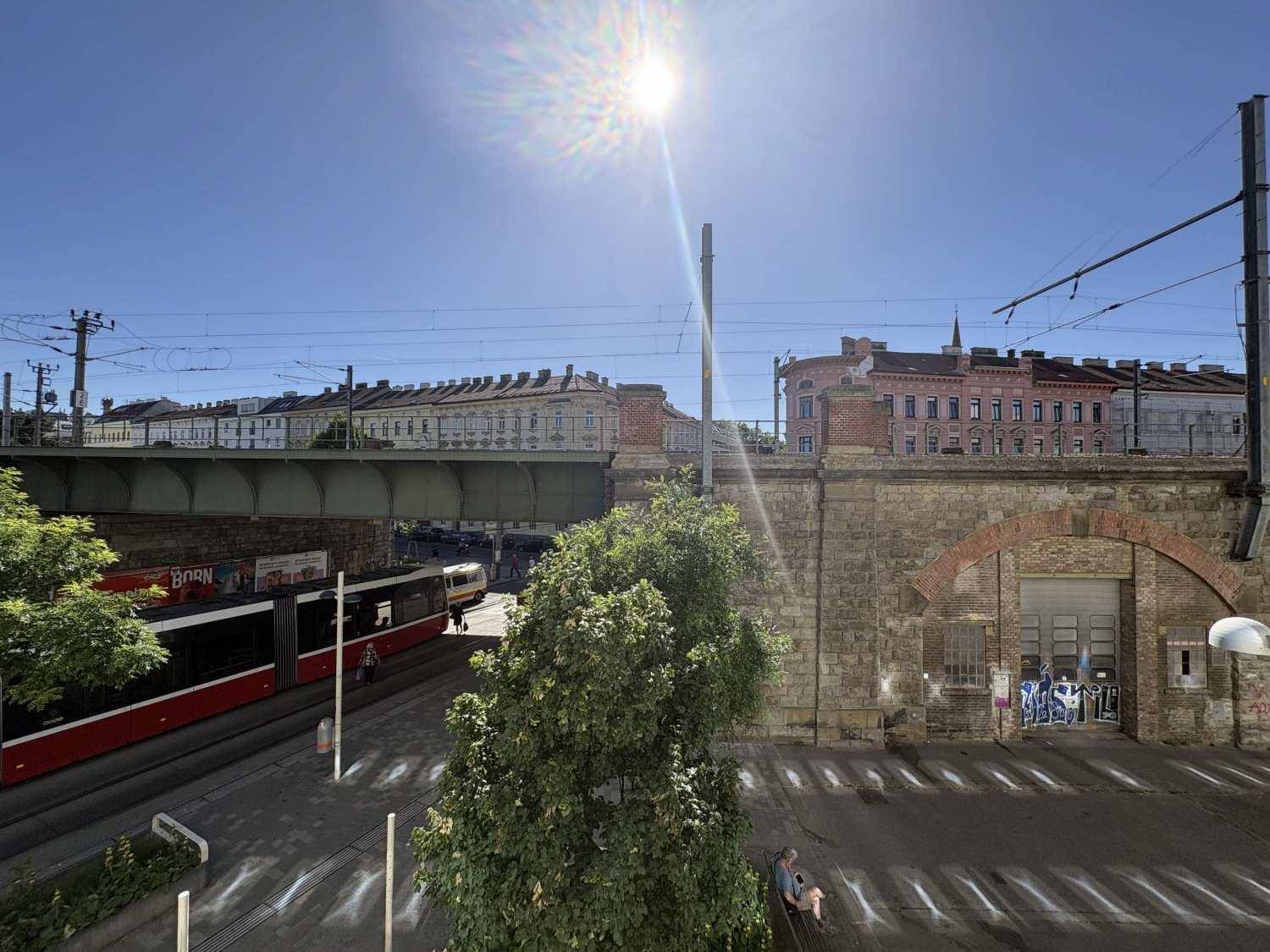 Blick auf eine belebte Straße mit Straßenbahn, einer Brücke und historischen Gebäuden im Hintergrund.