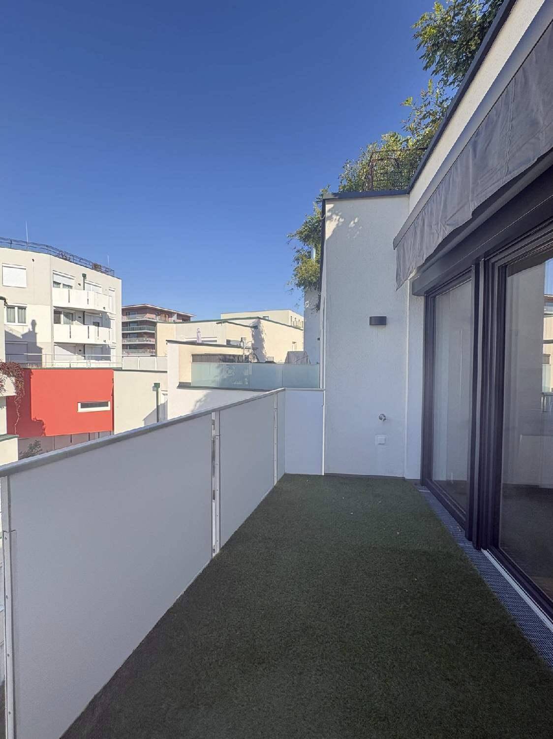 Balkon mit Kunstrasen und Blick auf die umliegende Bebauung unter blauem Himmel.