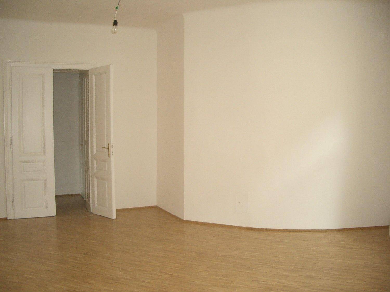 Heller Raum mit Parkettboden und weißen Wänden, inklusive einer eleganten Rundung und Doppeltür.