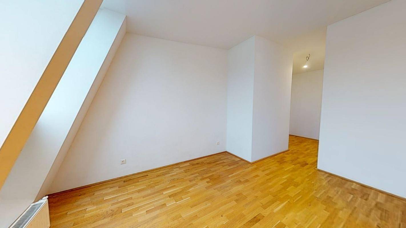 Leerer Dachgeschossraum mit Holzboden und schrägen Wänden, bereit zur Einrichtung.