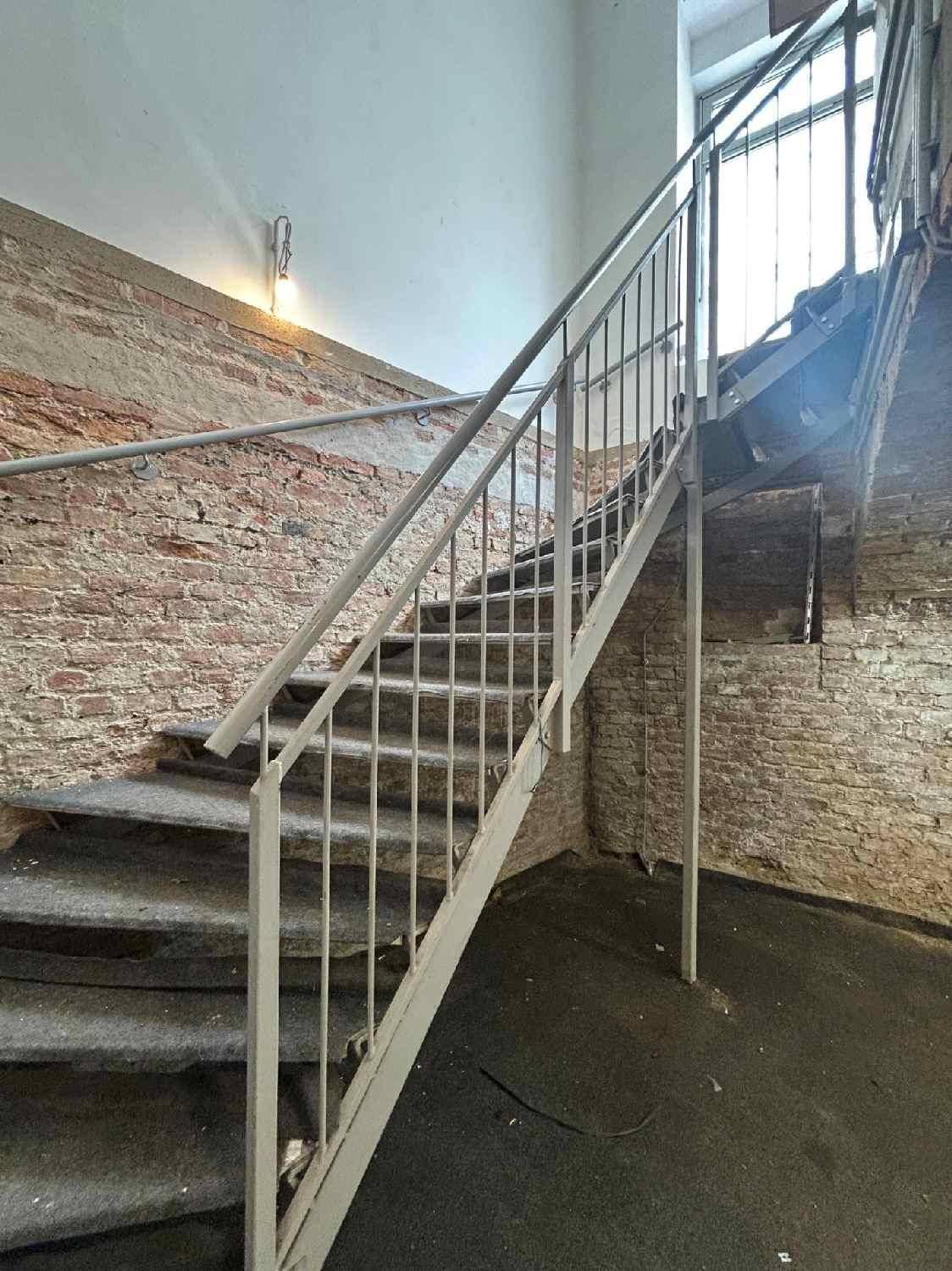 Robuste Metalltreppe in einem Bereich mit freiliegenden Ziegelwänden und einfacher Beleuchtung.