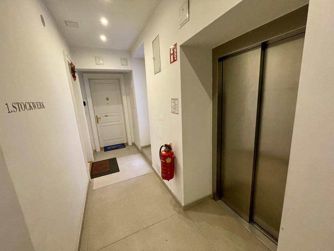 Heller Flur im ersten Stockwerk mit Aufzug und weißer Eingangstür zu einer Wohnung.