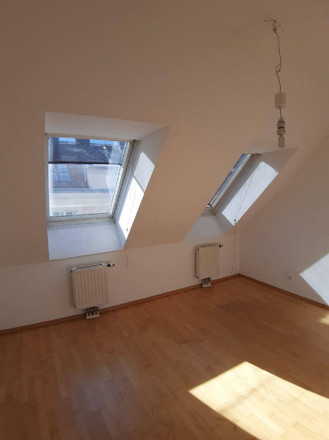Heller Dachgeschossraum mit Holzboden, zwei Dachfenstern und Heizkörpern, ideal für Wohnzwecke.