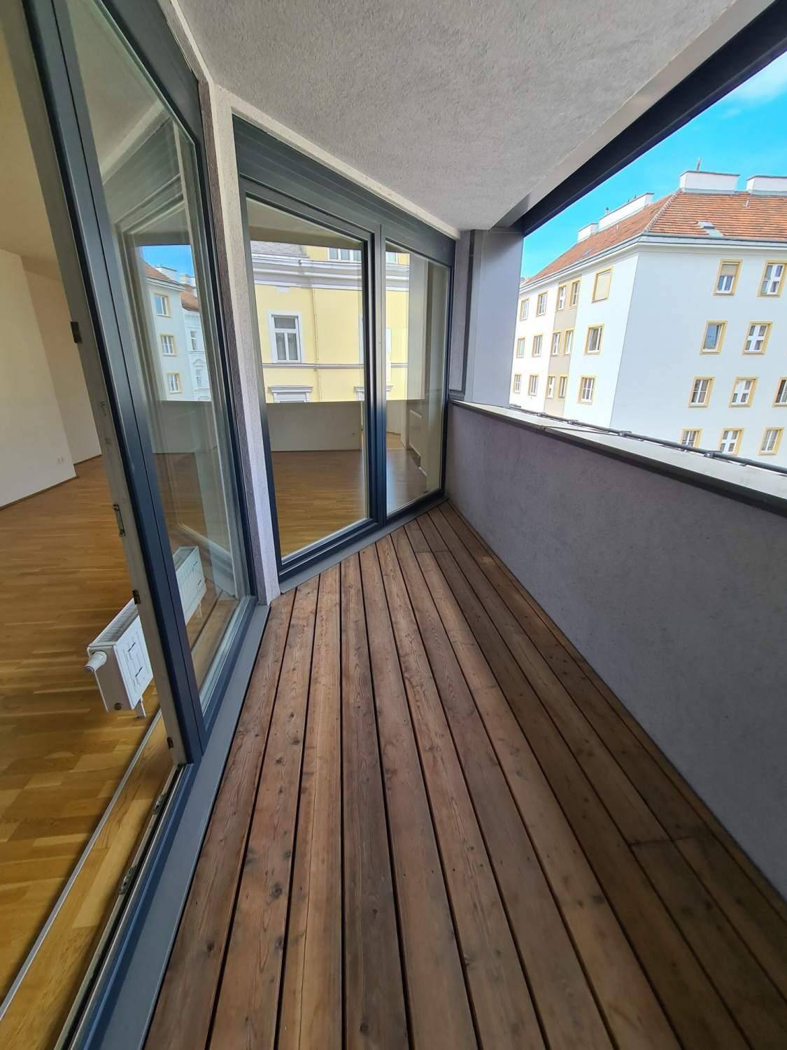 Geräumiger Balkon mit Holzdielen und Blick auf die umliegenden Stadtgebäude.