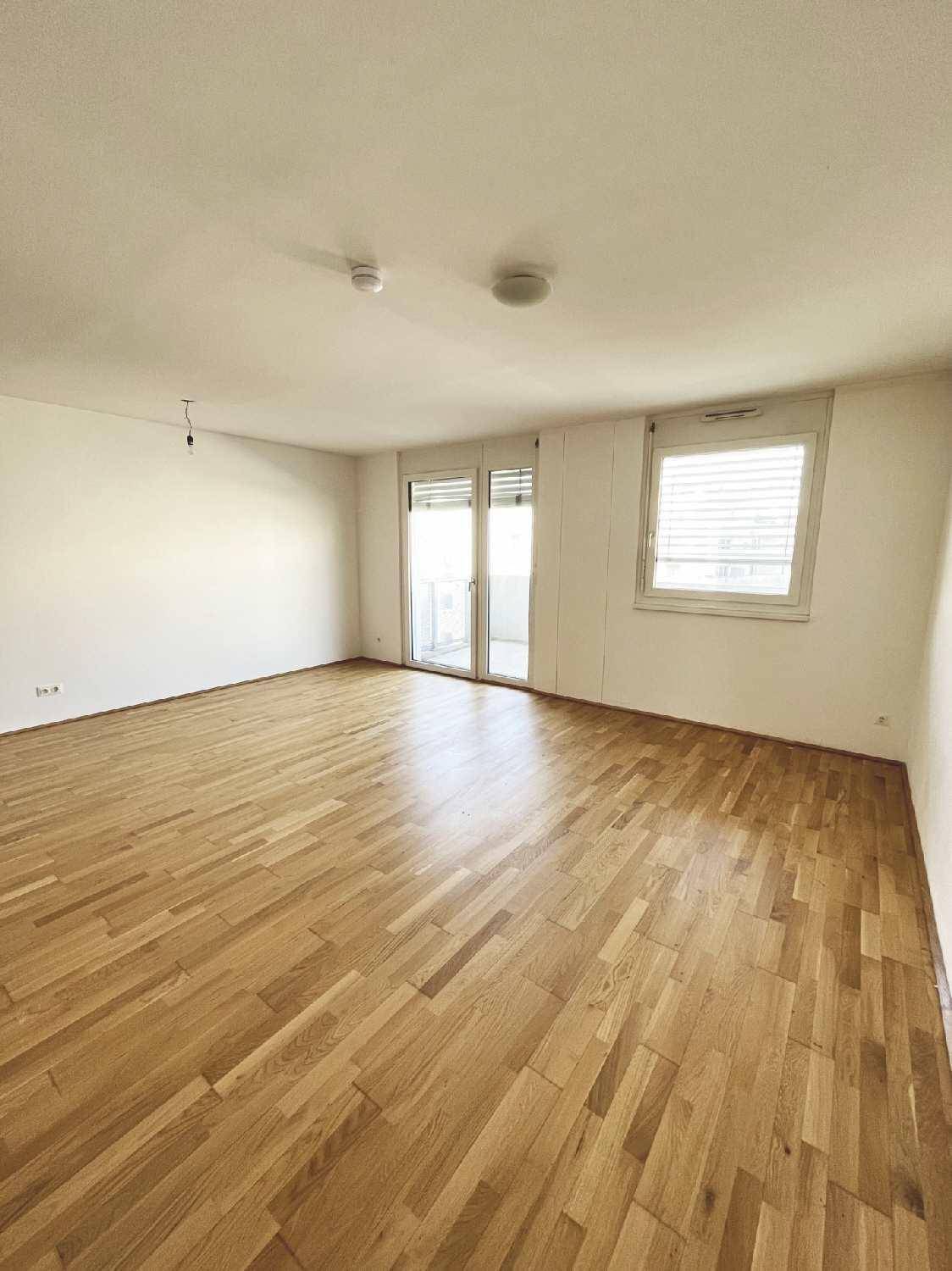 Heller Wohnraum mit Parkettboden, großen Fenstern und Zugang zu einem Außenbereich.
