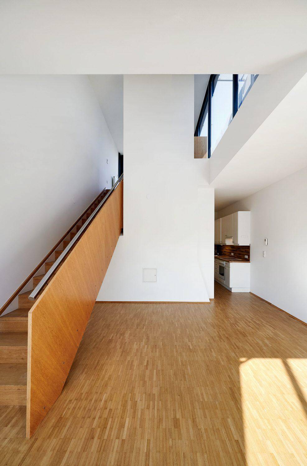 Geräumiger Wohnbereich mit Holzfußboden, offener Treppe und viel natürlichem Licht.