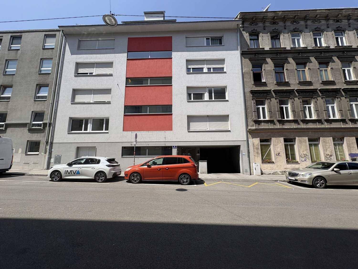 Mehrstöckiges Wohngebäude mit moderner Fassade und roten Akzenten an einer belebten Stadtstraße.