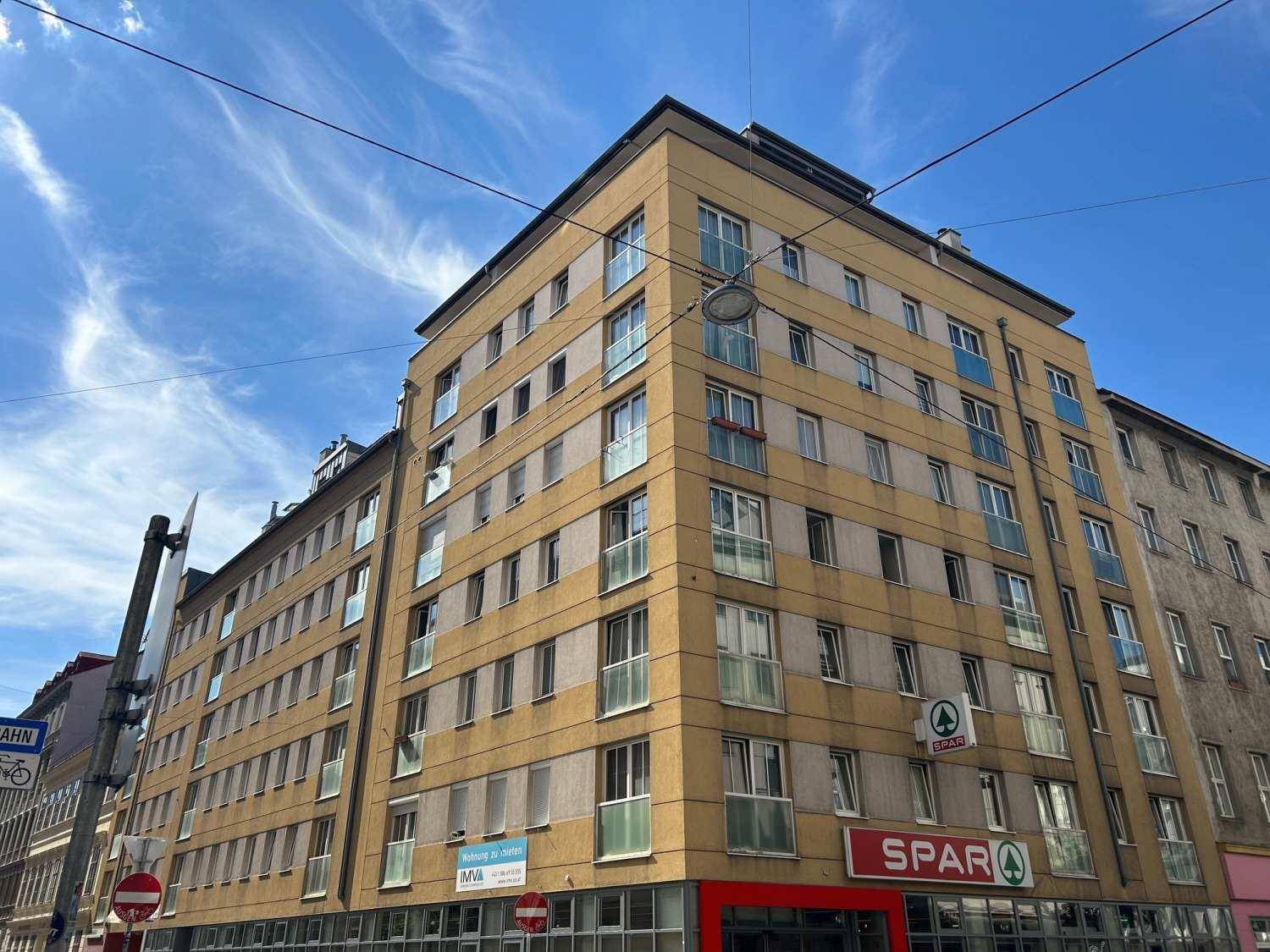 Eckansicht des Gebäudes mit gelber Fassade und einem SPAR Supermarkt im Erdgeschoss.