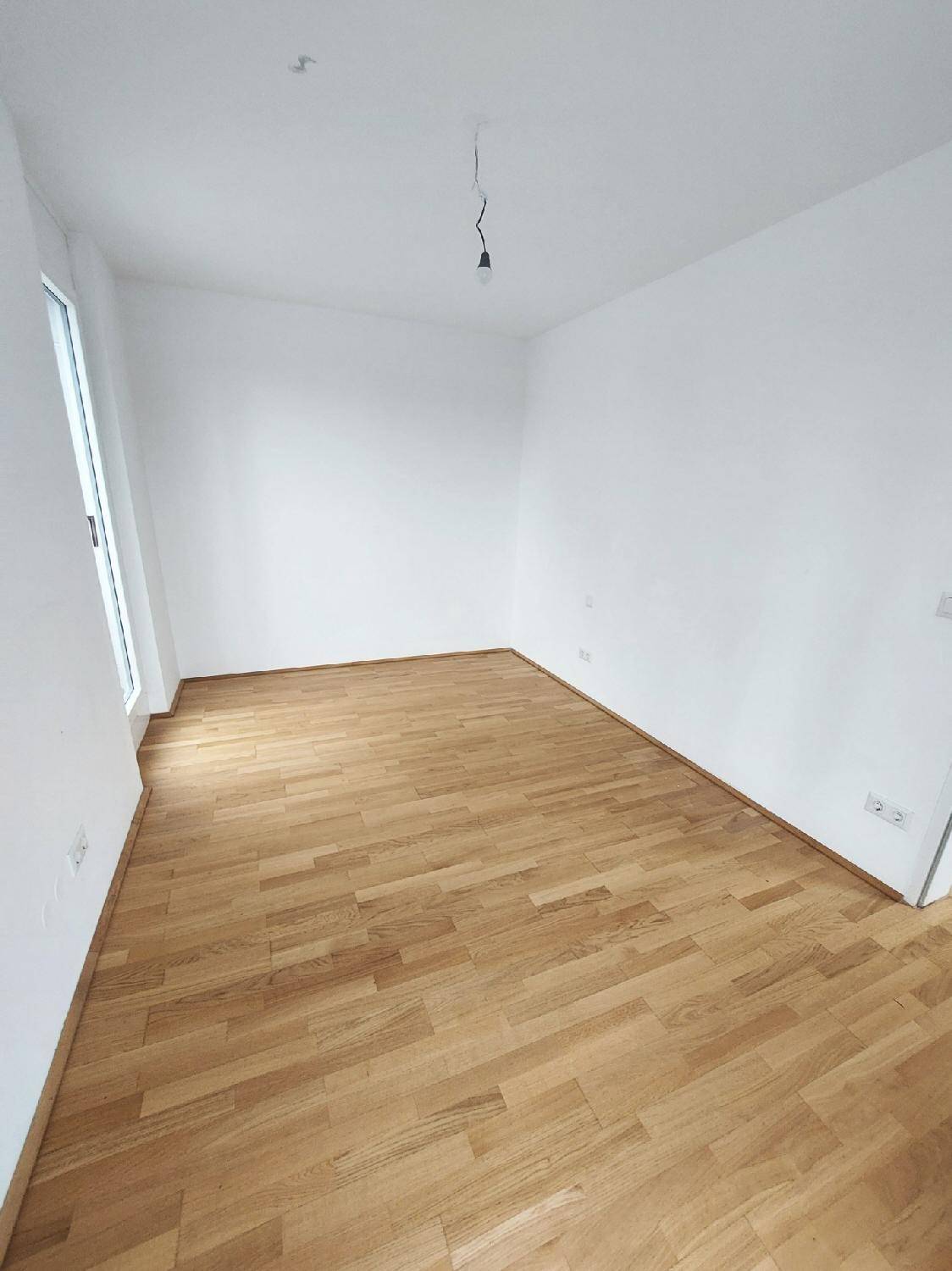 Leerer Raum mit hellem Parkettboden und weißen Wänden, bereit zur individuellen Gestaltung.