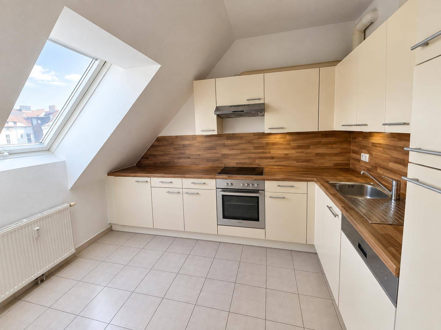 Moderne Einbauküche mit beigen Schränken, Holzarbeitsplatten und einem großen Dachfenster.