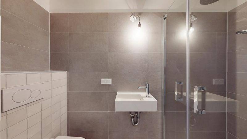 Modernes Badezimmer mit Duschkabine, Einzelwaschbecken und grauen Wandfliesen.