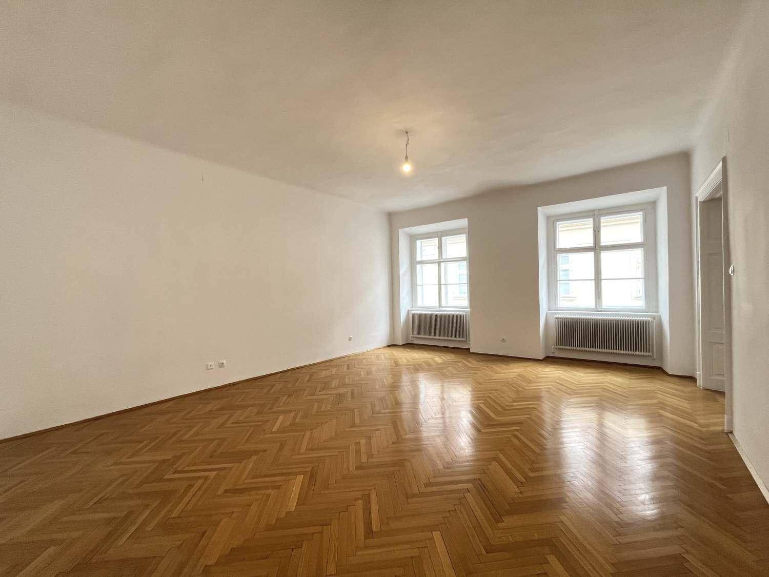 Großes, helles Zimmer mit Fischgrätparkett und zwei Fenstern, bereit zur individuellen Gestaltung.