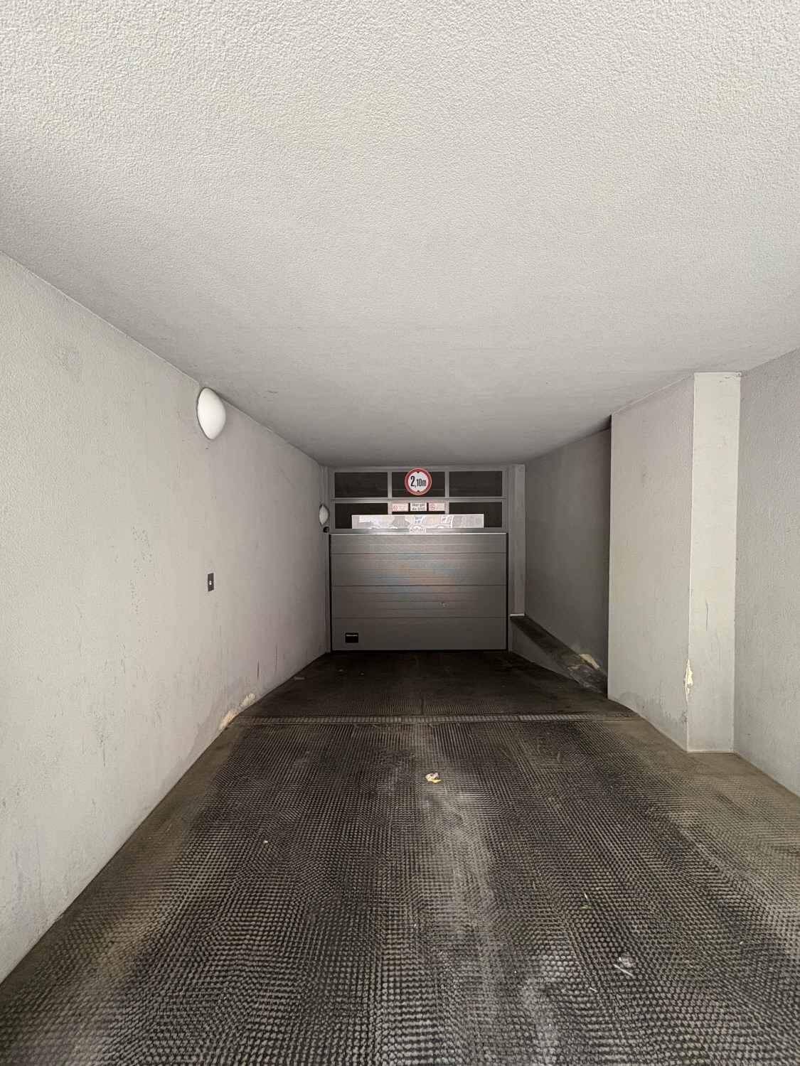 Leere Garagenbox mit geschlossenem Rolltor und einer Höhenbegrenzung von 2,10 Metern.