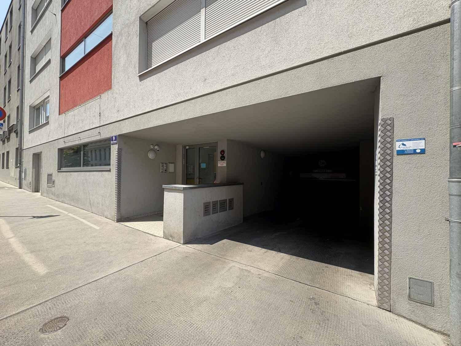 Eingangsbereich einer Tiefgarage mit Zufahrt von der Straße und moderner Fassadengestaltung.