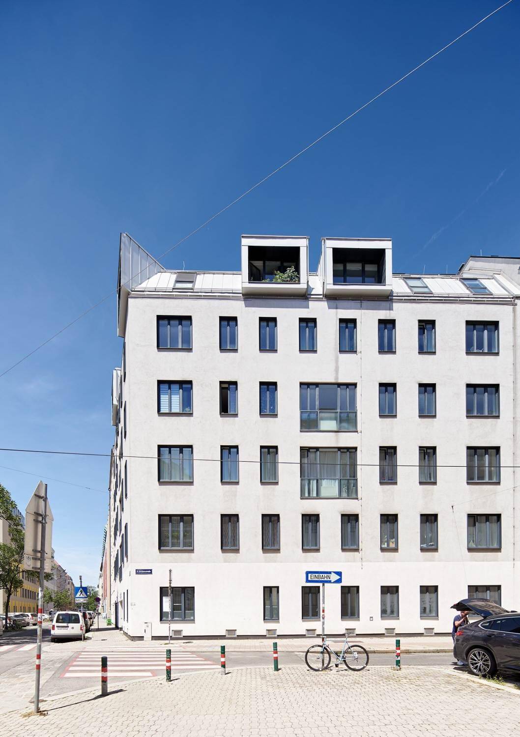 Weißes Mehrfamilienhaus mit moderner Architektur und vielen Fenstern unter blauem Himmel.