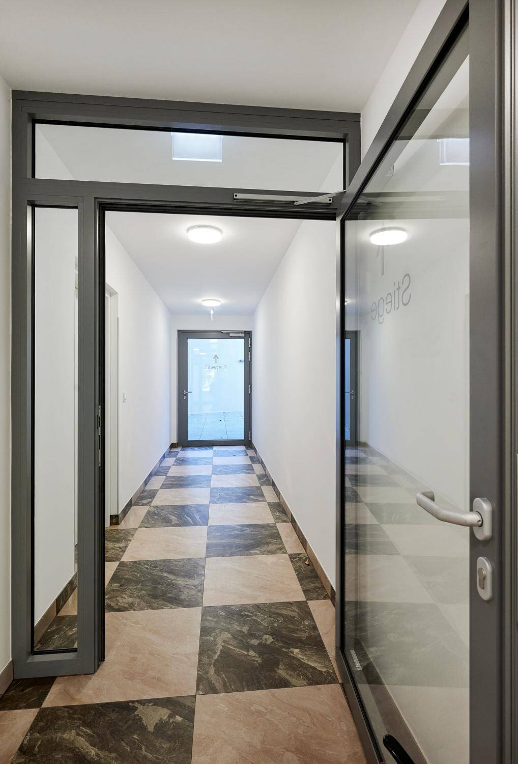 Heller Gemeinschaftsflur mit gemustertem Fliesenboden und Glastüren.