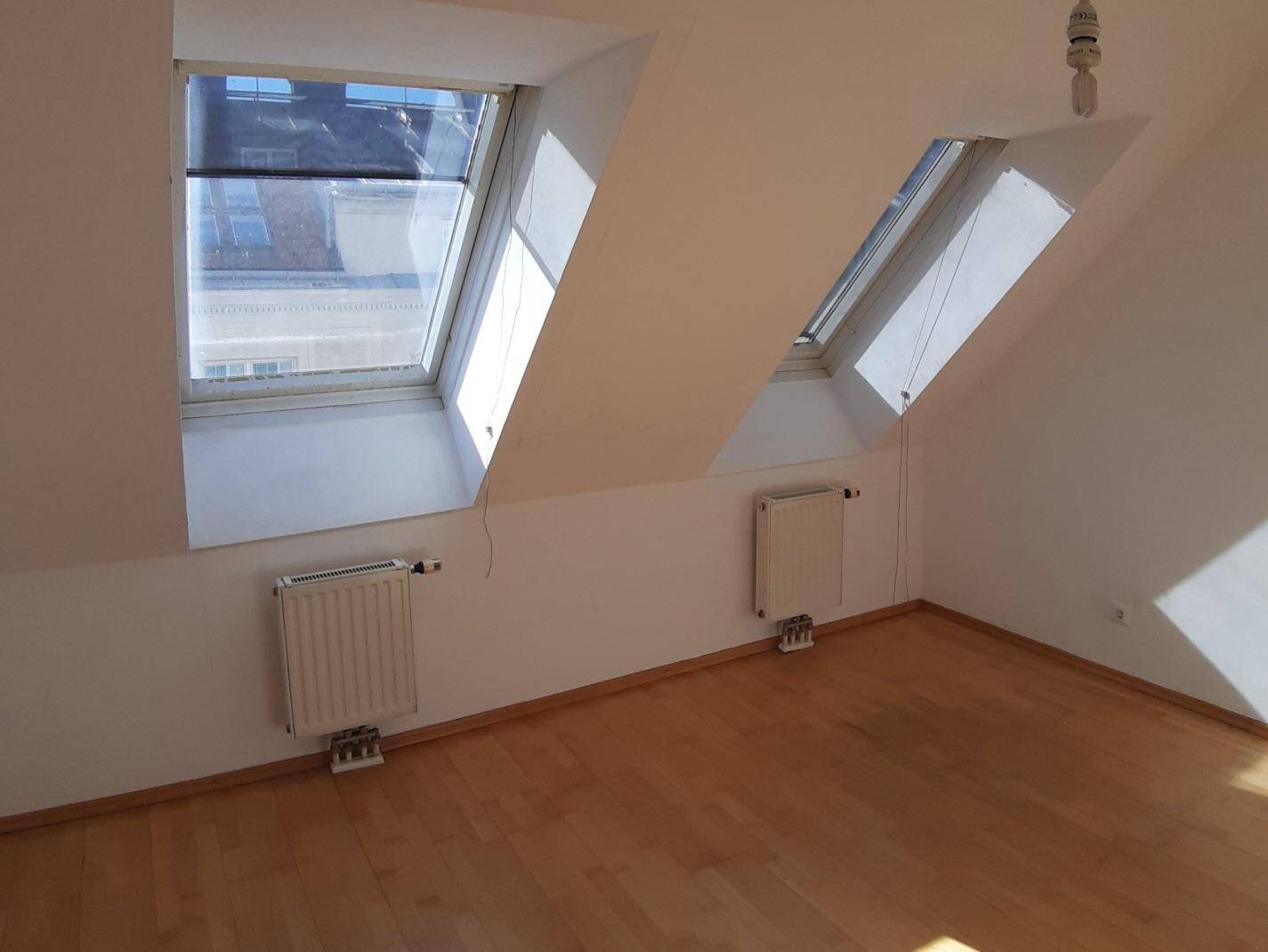 Heller Raum im Dachgeschoss mit zwei Dachfenstern, Heizkörpern und Holzboden.