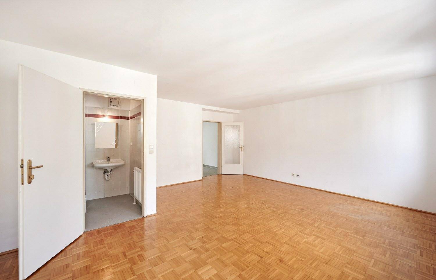 Heller Wohnraum mit Parkettboden und direktem Zugang zu einem kleinen Badezimmer.