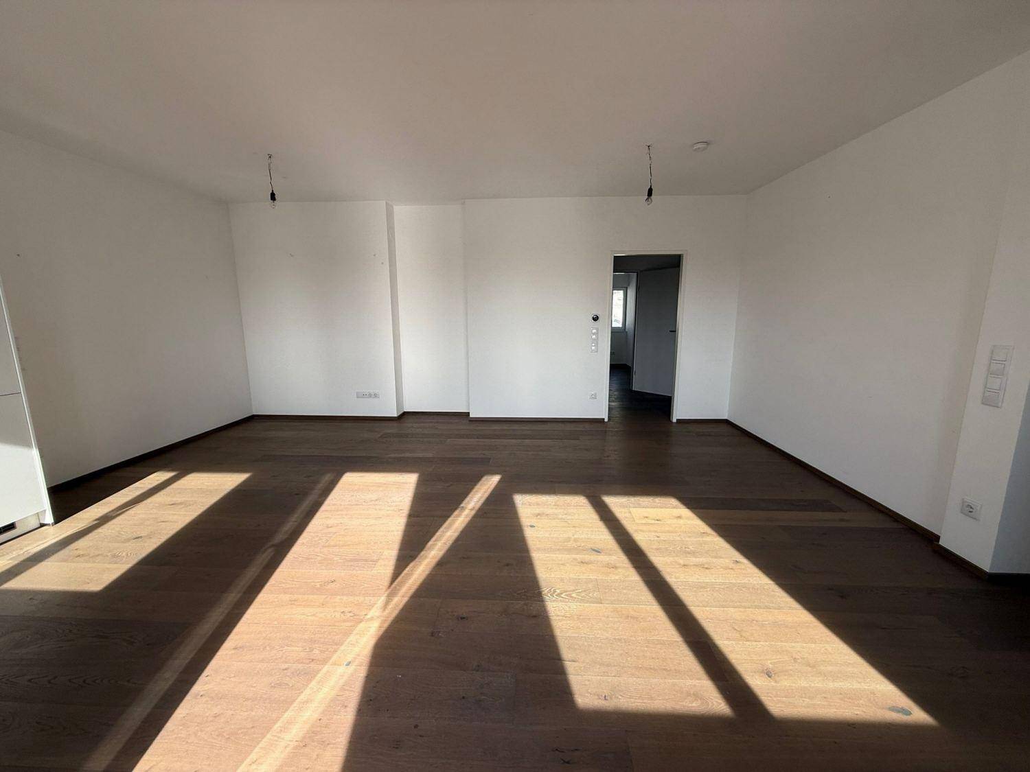 Geräumiger, heller Wohnbereich mit Holzboden und weißen Wänden, durchflutet von Sonnenlicht.